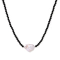 Beaded black agate necklace with iridescent baroque freshwater pearl centerpiece on cream background.