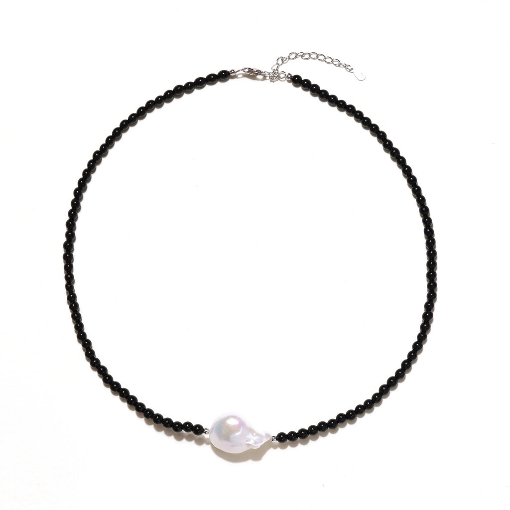 Beaded black agate necklace with iridescent baroque freshwater pearl centerpiece on cream background.