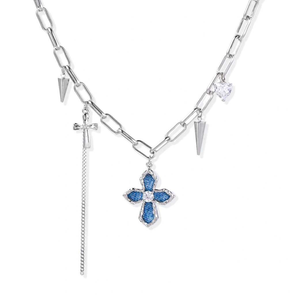 White gold plated chain necklace with blue textured cross pendant, spike charms, and mini cross detail on beige background