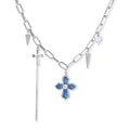 White gold plated chain necklace with blue textured cross pendant, spike charms, and mini cross detail on beige background
