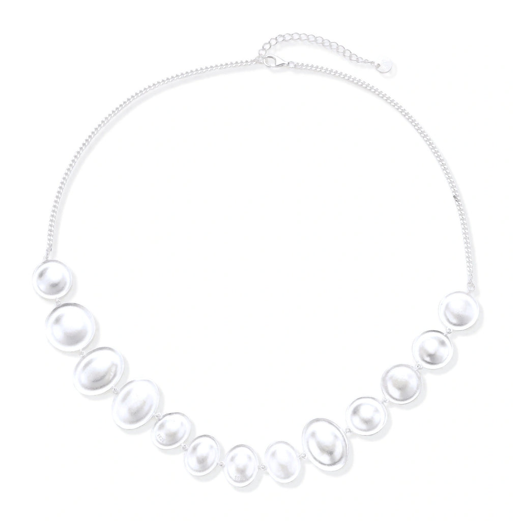 Graduated pearl-finish silver discs forming an organic bubble bib necklace on delicate chain against cream background.