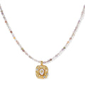 Ornate gold-plated pendant necklace with multicolored gemstone beads in purple, pink and clear tones on white background