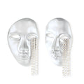Silver face-shaped statement earrings with flowing chain tassels hanging from sculpted lips on cream background