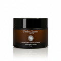 A 50mL jar of Timeless Organics Skin Care Exfoliating Cream Cleanser, featuring a dark amber brown jar and a glossy black lid, set against a warm beige background with soft diagonal light shadows.