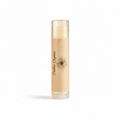 A single tube of lip balm standing upright on a reflective beige surface, with a warm cream-colored balm visible inside a clear tube and a kraft-paper style label reading 'Tenderlass Organics' with a dandelion illustration.