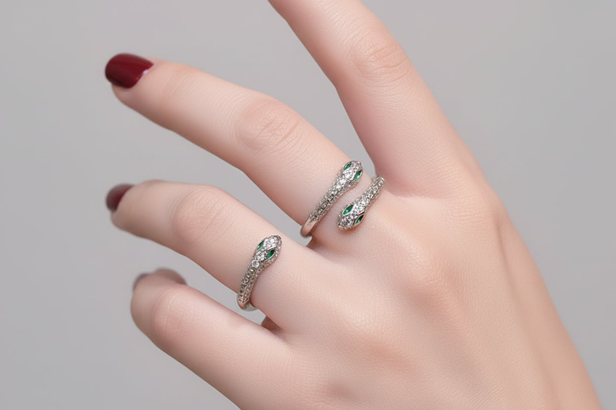 Close-up of a hand wearing two silver snake-shaped rings with green gemstones on a fluffy white surface.