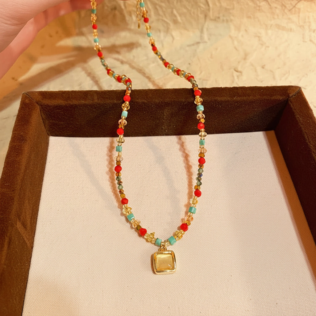 Colorful beaded necklace with a gold pendant on a pink cushion, with a label underneath.