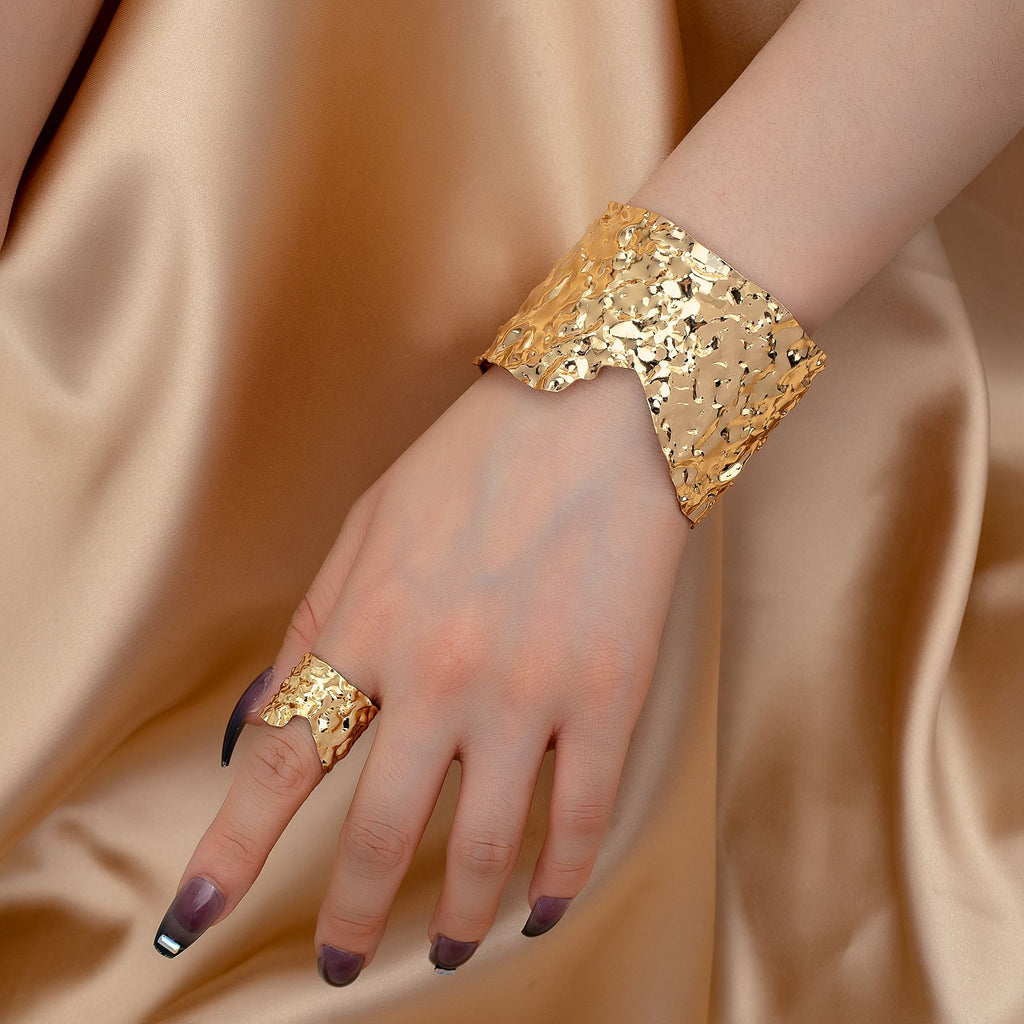 Gold bracelet and ring on a hand against a beige fabric background