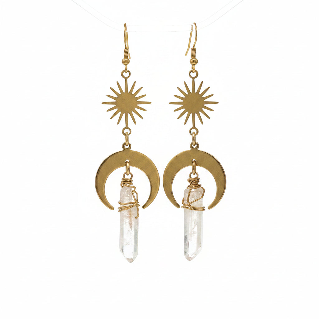 Gold earrings with sun and moon designs and clear gemstones on a wooden surface