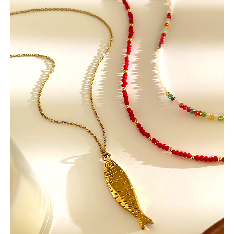 Gold fish pendant necklace and red beaded necklace on a white surface