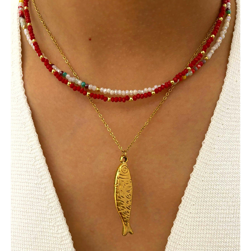 Gold fish pendant necklace on a person wearing a white top