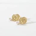 Gold floral earrings with pearls on a beige cushion