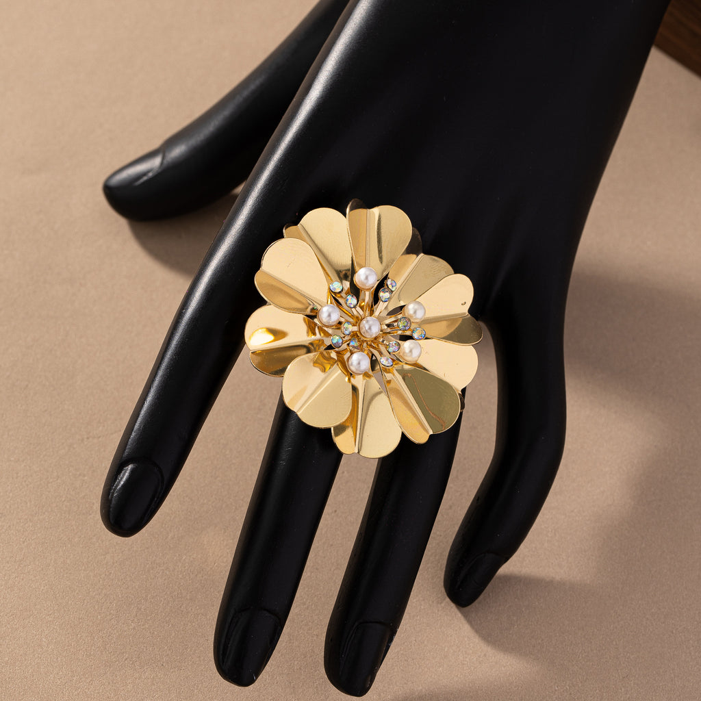 Gold floral ring with pearl accents on a black-gloved hand against a beige background
