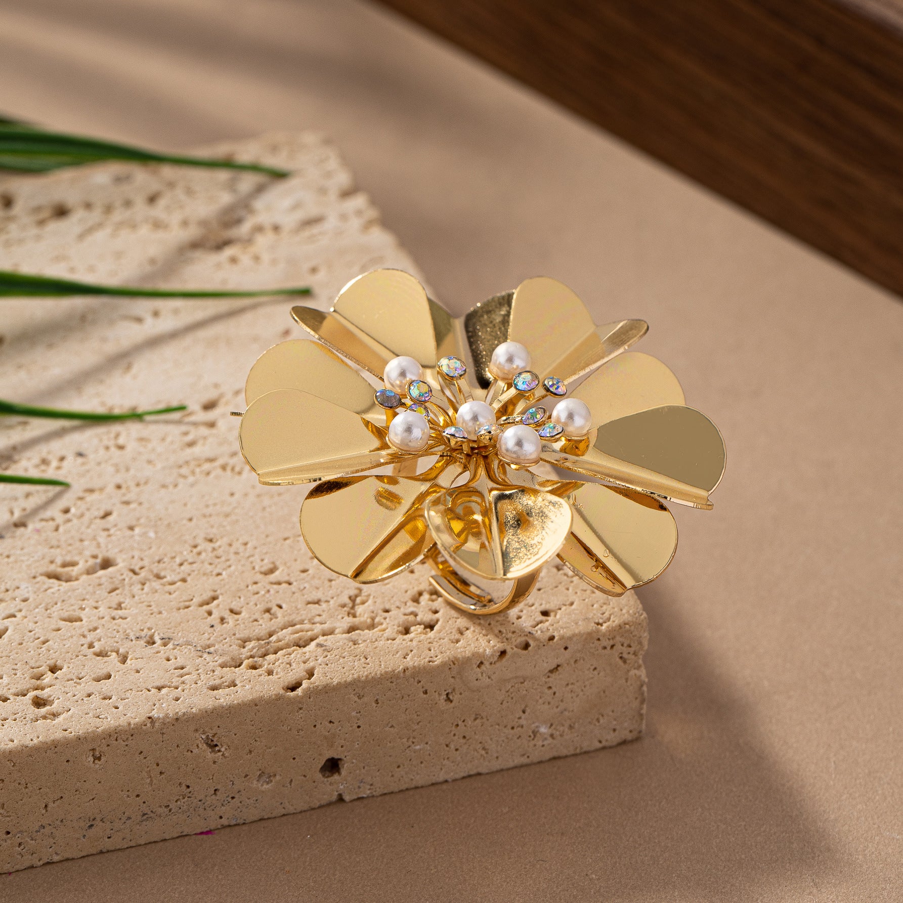 Gold flower-shaped brooch with pearls and gemstones on a beige surface