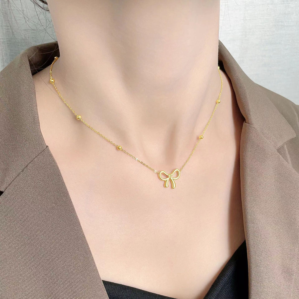Gold necklace with a bow pendant on a person wearing a brown blazer.
