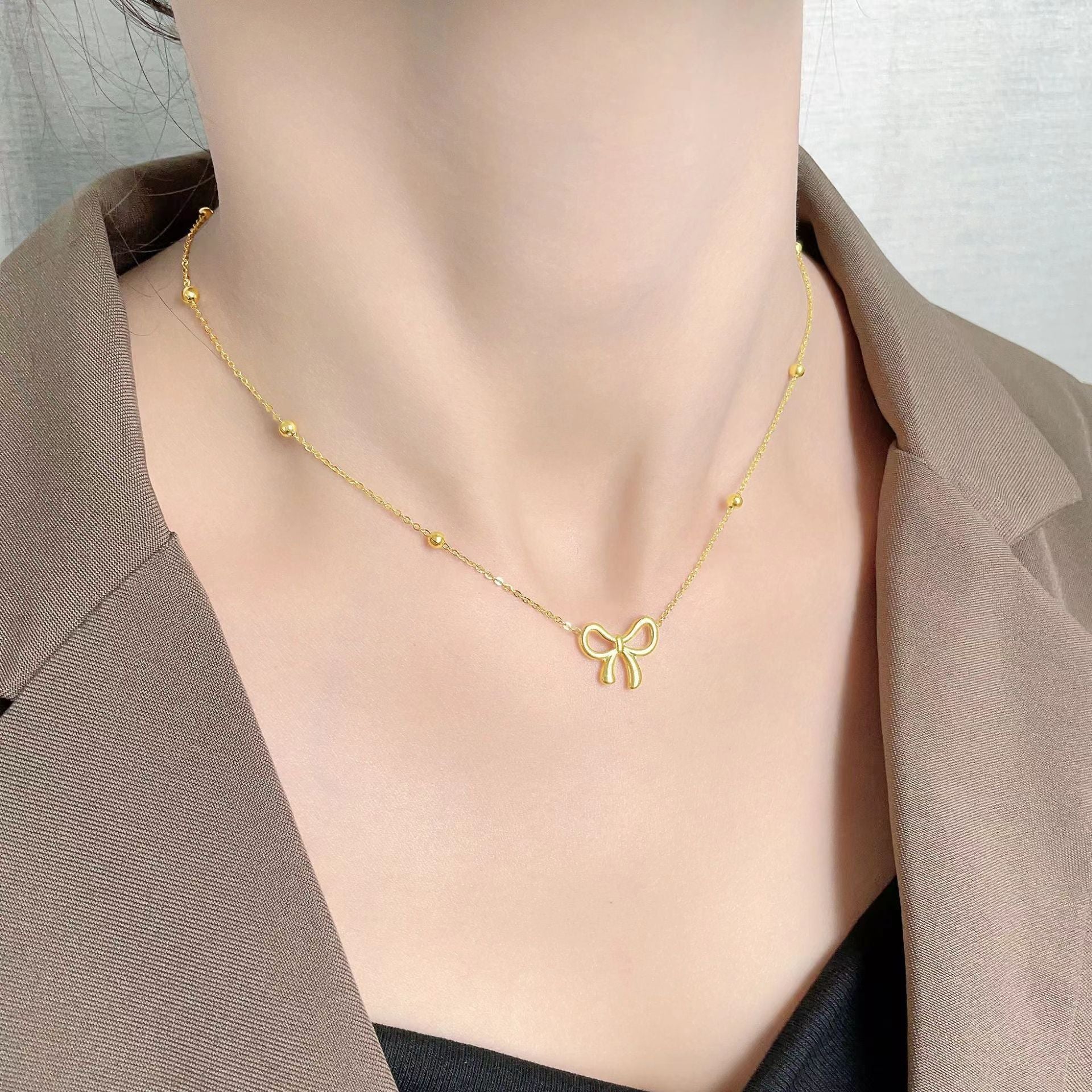 Gold necklace with a bow pendant on a person wearing a brown blazer.
