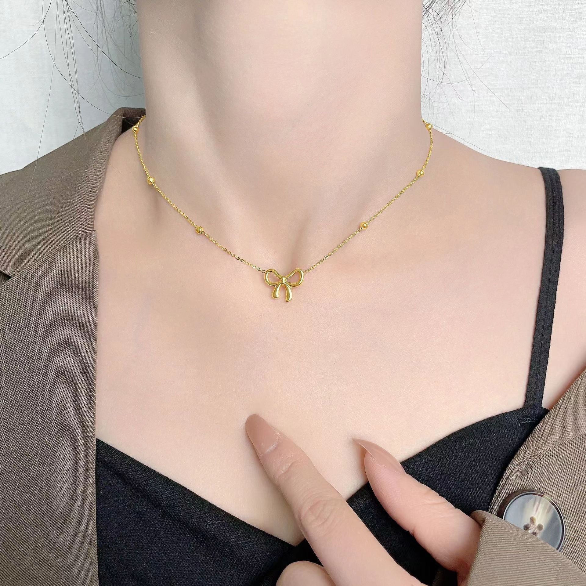 Gold necklace with a bow pendant worn by a person, pointing to the necklace.