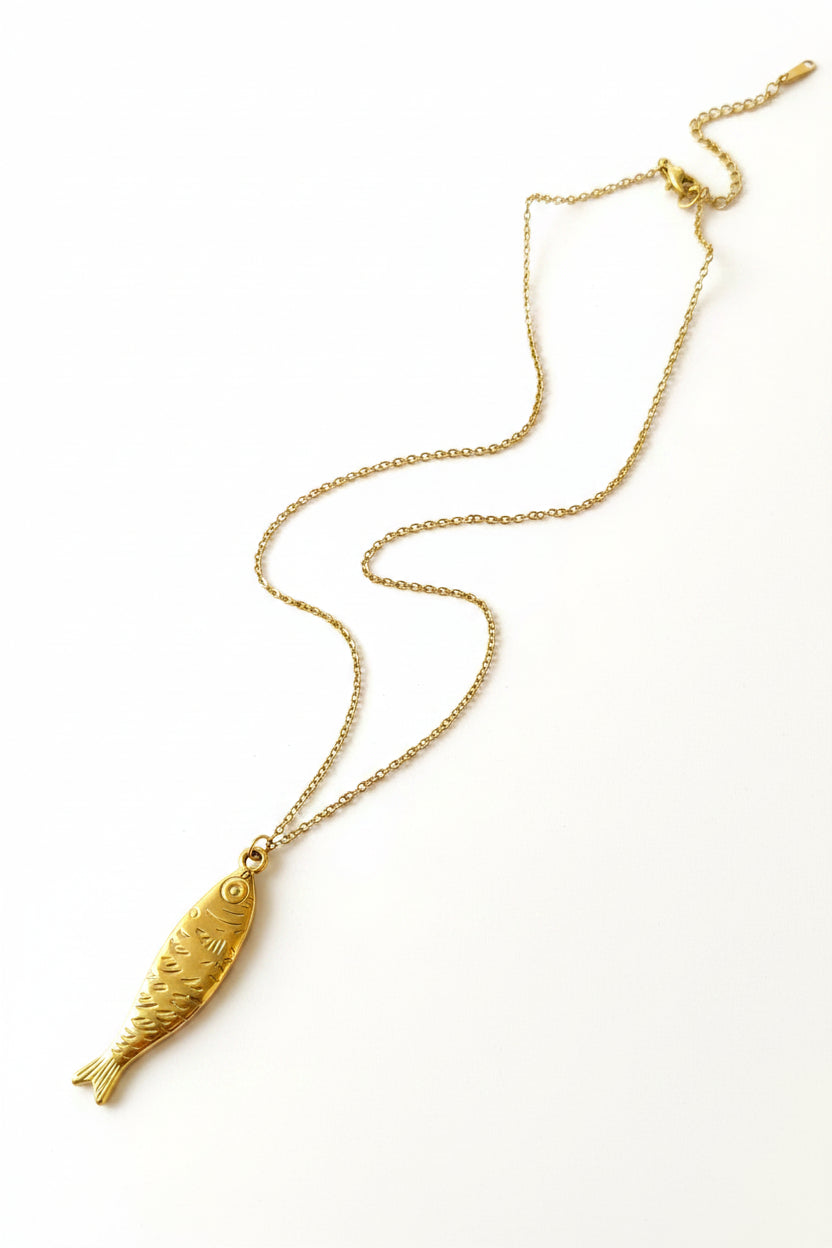 Gold necklace with a fish pendant on a light surface