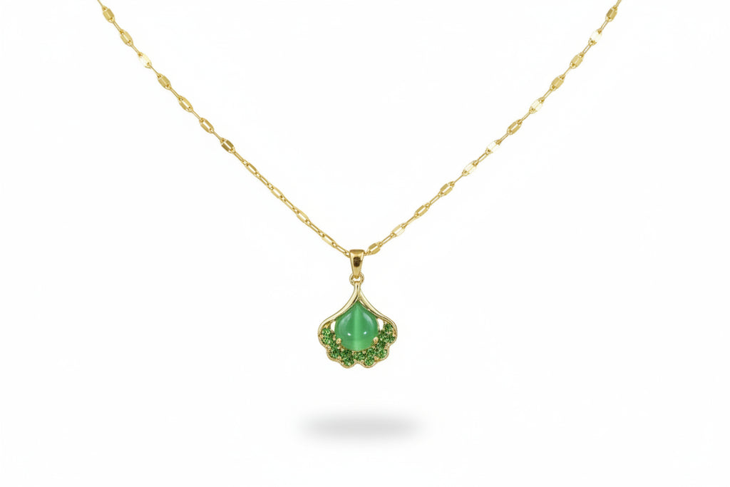 Gold necklace with a green pendant on a person wearing a brown top.