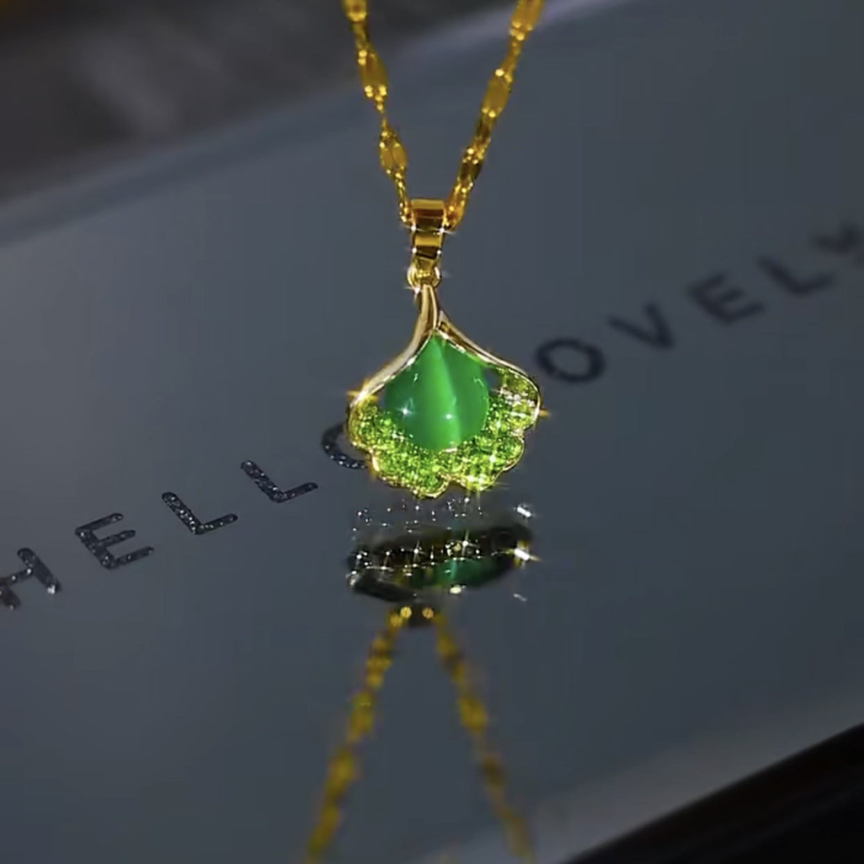 Gold necklace with a green pendant on a reflective surface