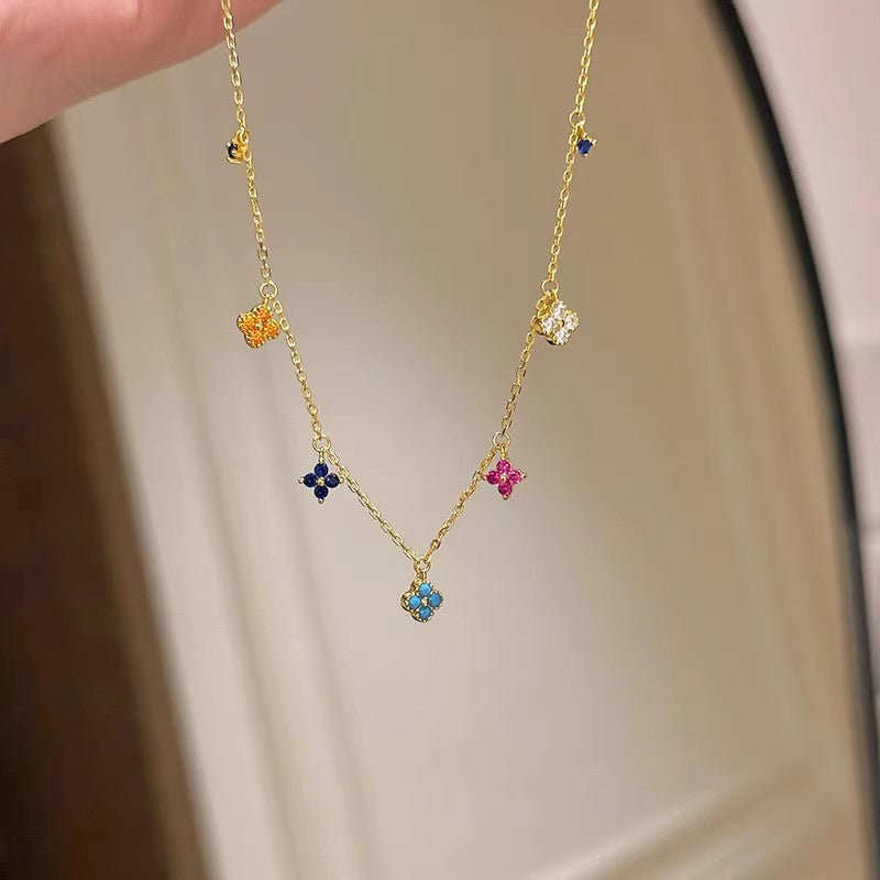 Gold necklace with colorful flower-shaped pendants on a neutral background