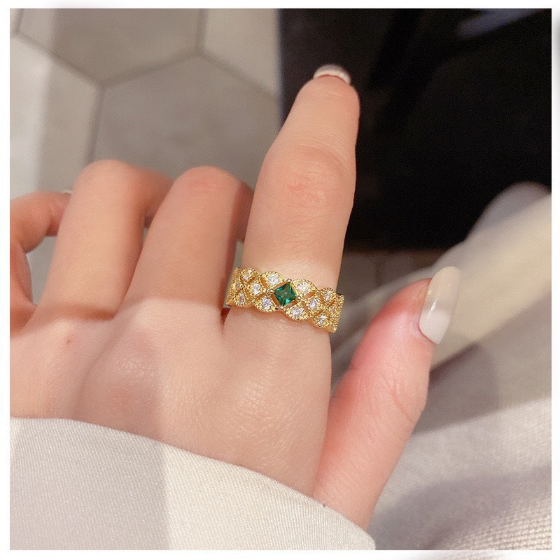 Gold ring with a green gemstone on a finger against a neutral background