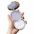 Hand holding a compact powder with a mirror on a beige background
