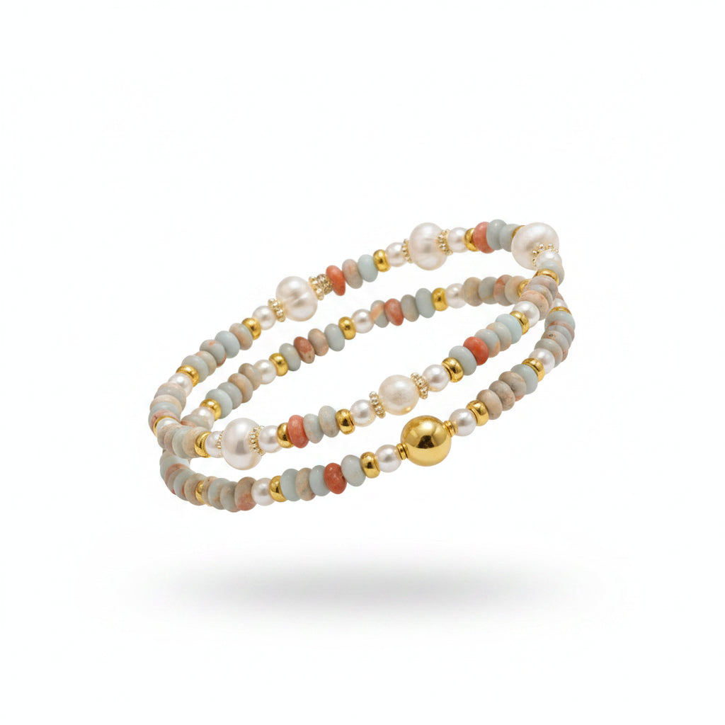 Hand wearing a beaded bracelet with pearls and gold accents on a neutral background