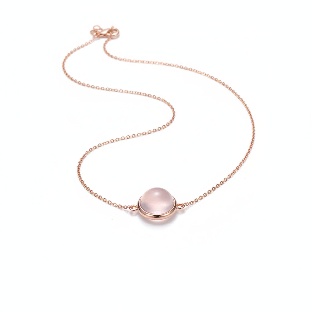 Hand wearing a necklace with a pink pendant against a neutral background