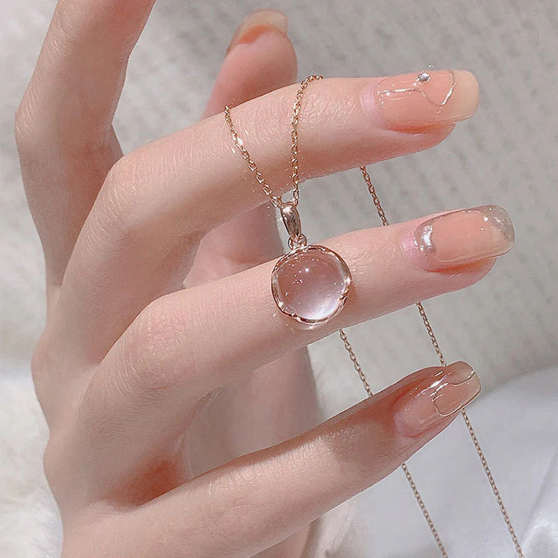 Hand wearing a necklace with a pink pendant against a neutral background