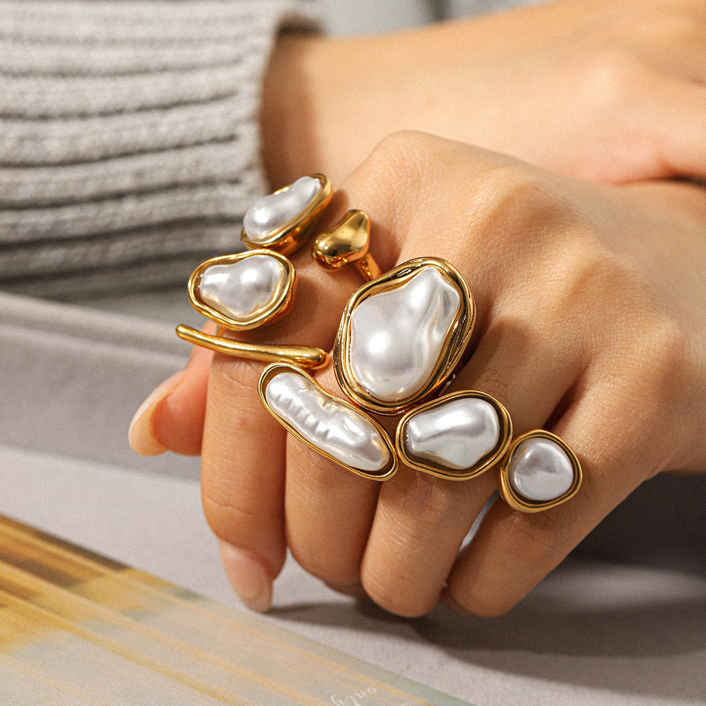 Hand wearing multiple gold and pearl rings on a neutral background