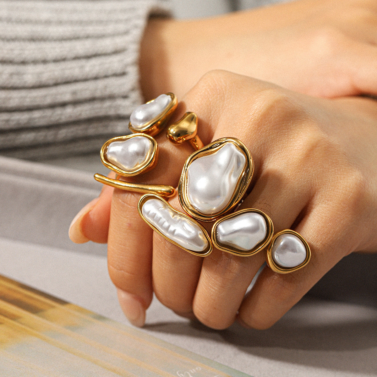 Hand wearing multiple gold and pearl rings on a neutral background