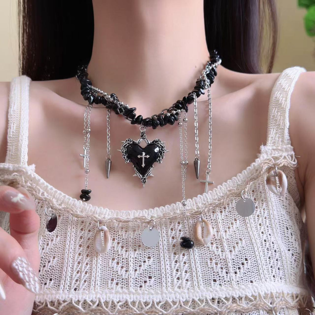 Necklace with a black heart and cross pendant worn by a person in a white lace top.
