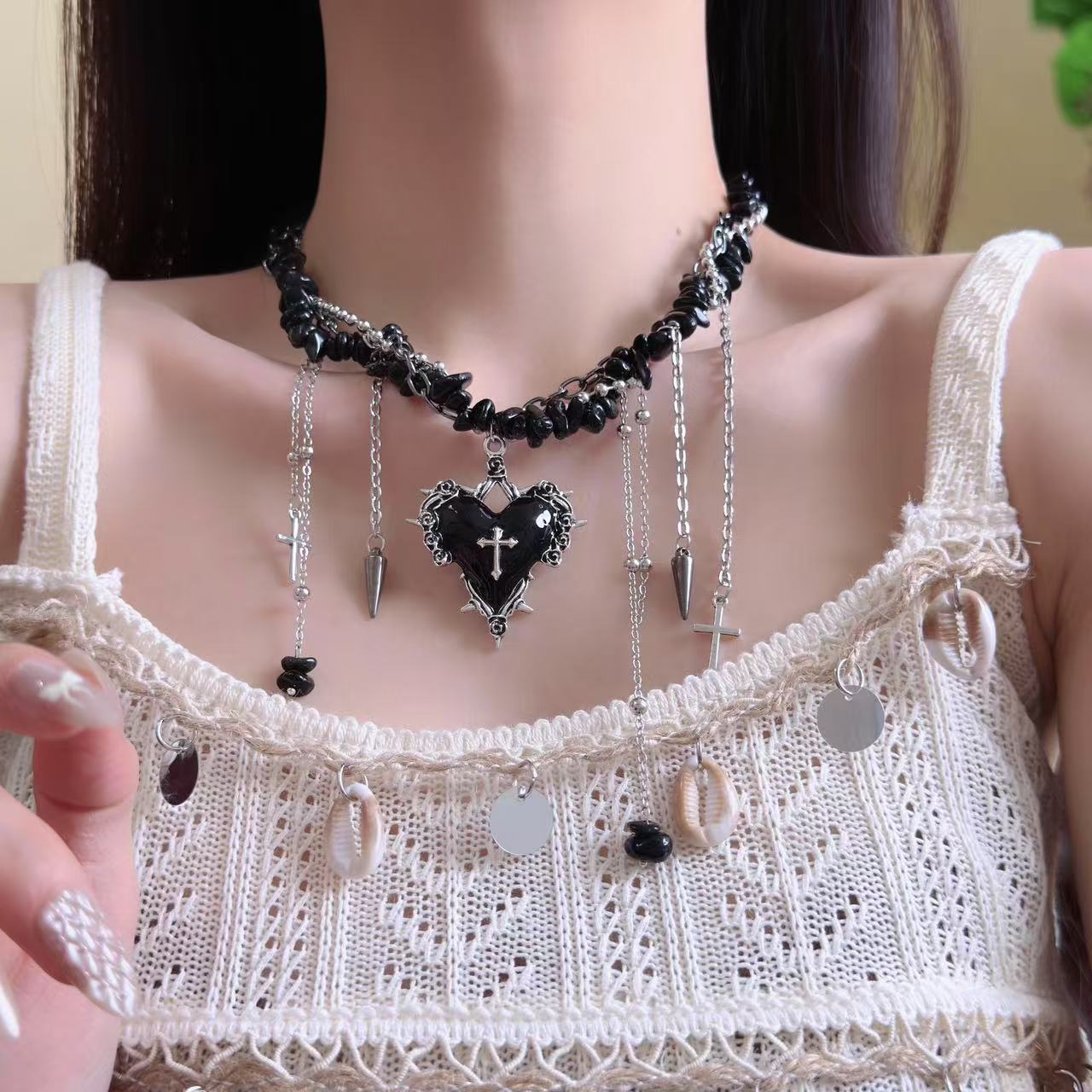 Necklace with a black heart and cross pendant worn by a person in a white lace top.