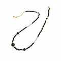 Necklace with black and gold beads on a wooden stand with a card underneath
