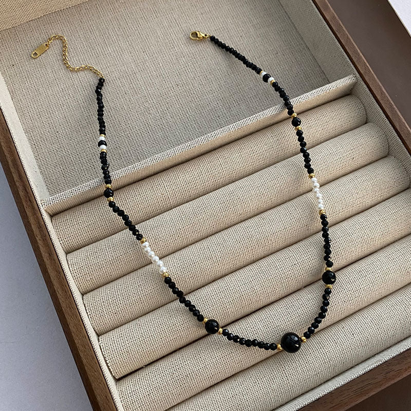 Necklace with black beads worn by a person in a denim shirt.
