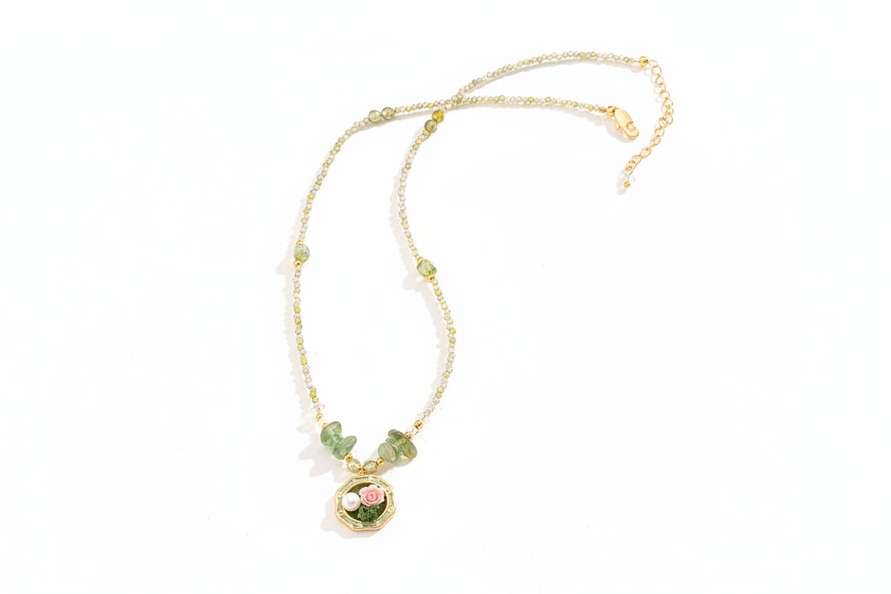 Necklace with green gemstones and a floral pendant on a light background