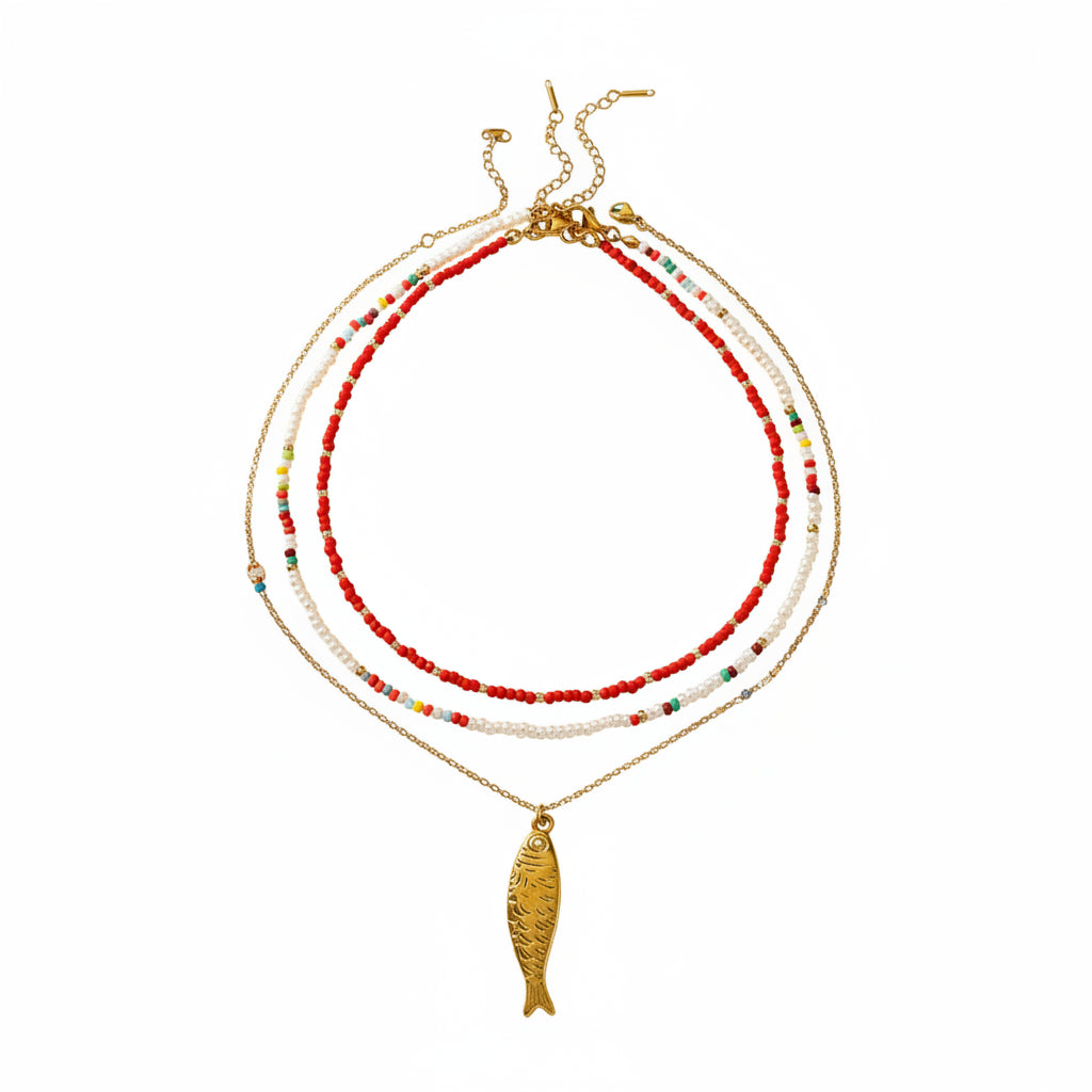 Necklace with red beads, gold fish charm, and pearl-like strands on a white background