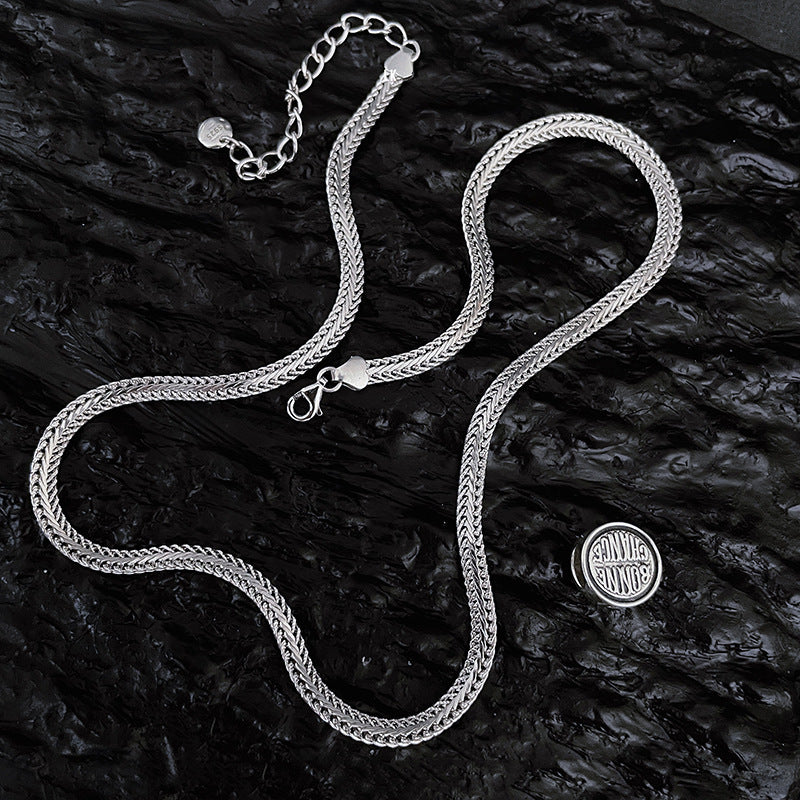 Silver chain necklace on a dark textured surface with a visible brand logo.