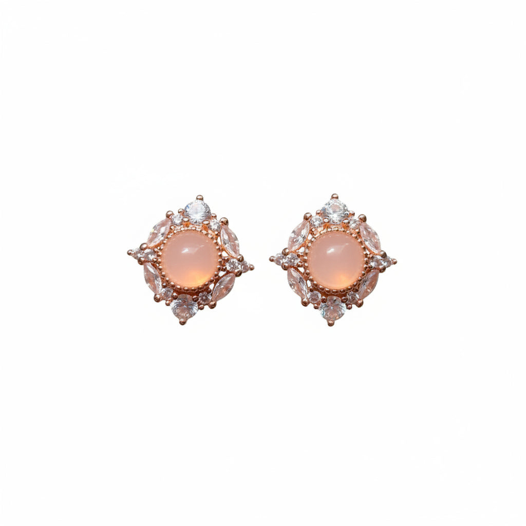 Pair of ornate earrings held between fingers with pink flowers in the background