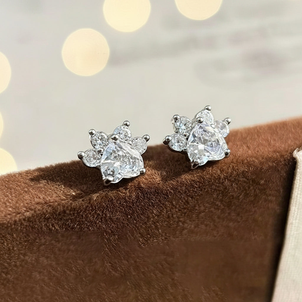 Pair of silver cat paw earrings on a brown surface with a blurred background