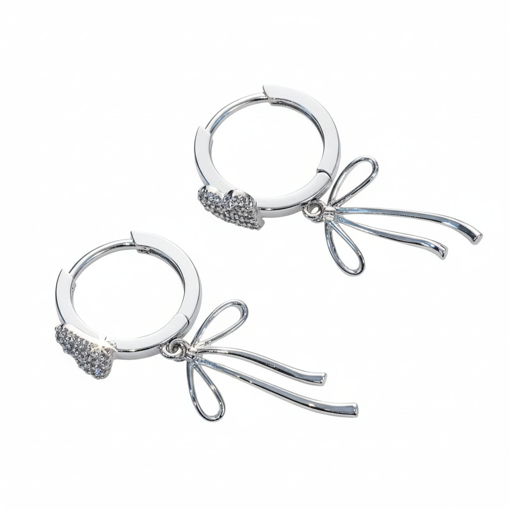Pair of silver hoop earrings with bow and heart charms on a white surface.