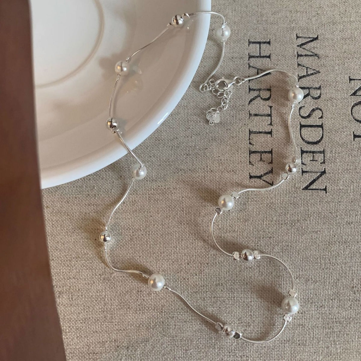Pearl necklace on a textured surface with 'Marsden Hartley' branding.