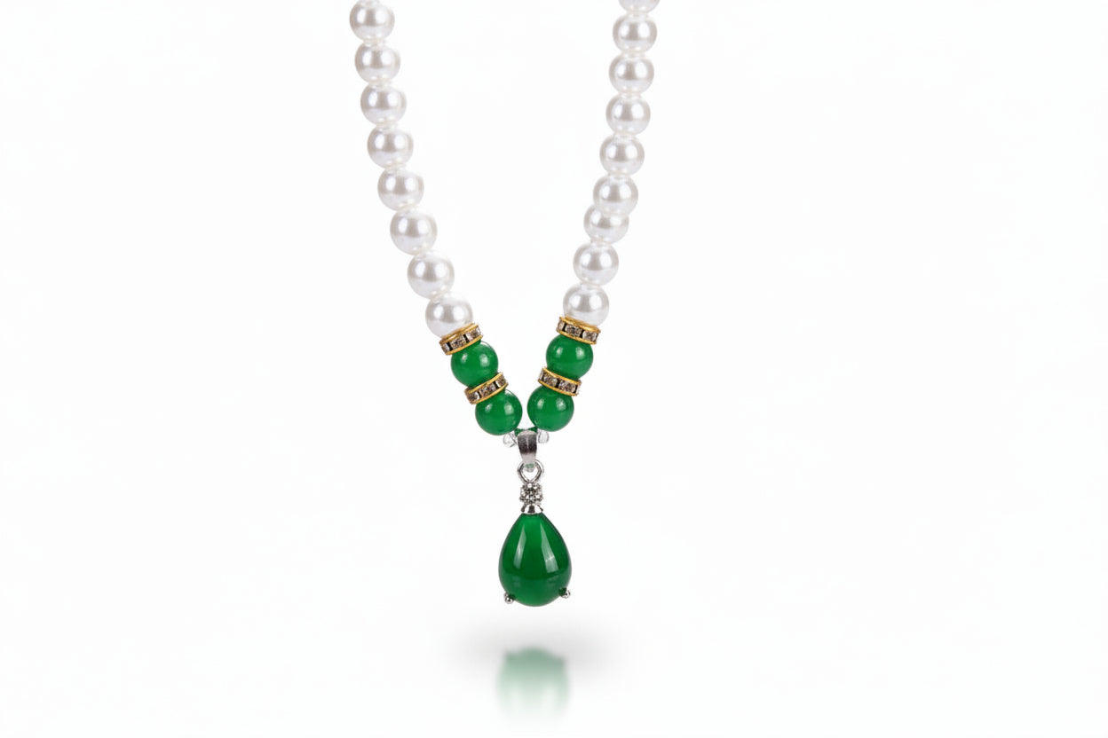 Pearl necklace with green beads and teardrop pendant, paired with pink teardrop earrings on a red background.
