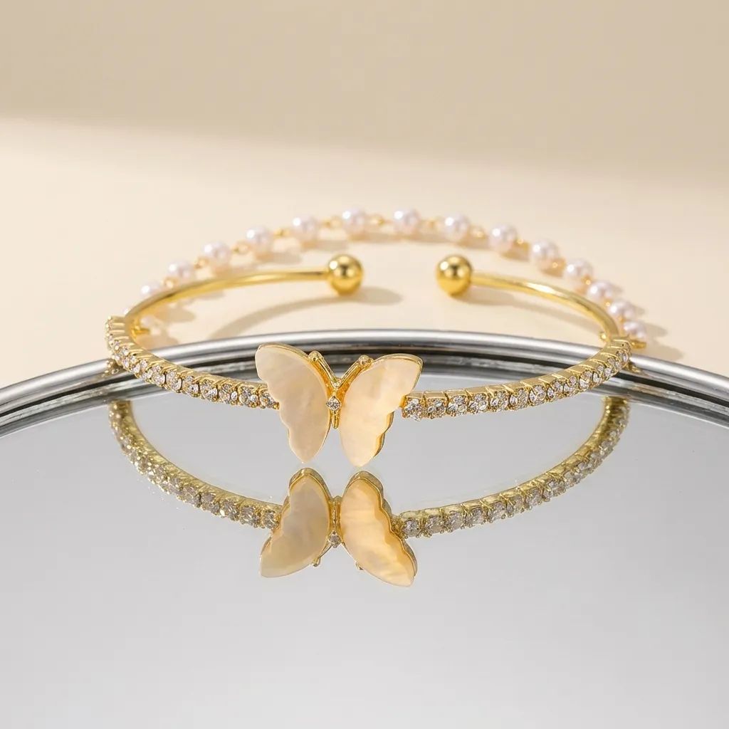 Set of gold butterfly-themed bracelets on a reflective surface with a neutral background
