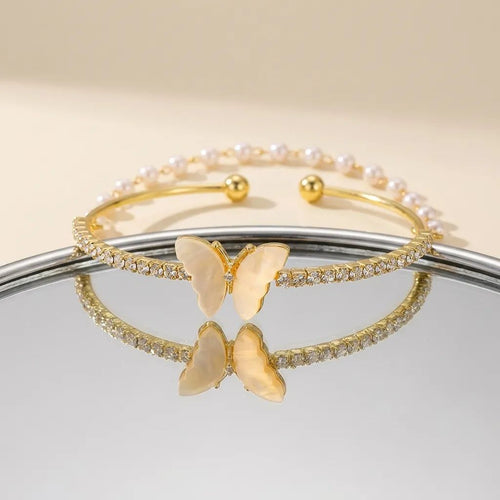 Set of gold butterfly-themed bracelets on a reflective surface with a neutral background
