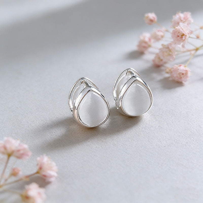 Silver earrings with clear stones on a light gray background with pink flowers.