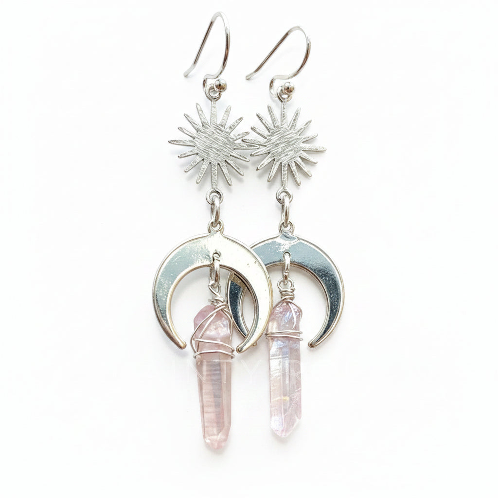 Silver earrings with moon phases and pink crystal drops on a wooden surface