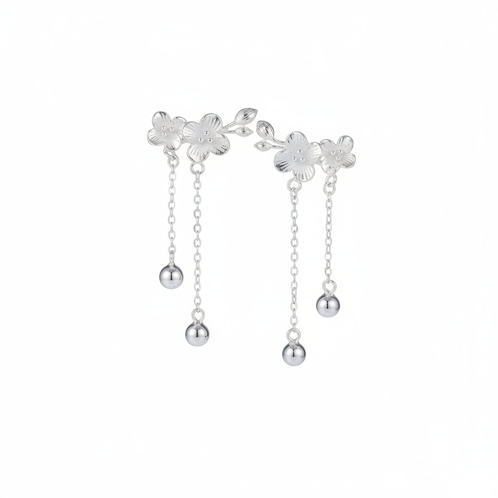 Silver floral earrings with chain and pearl details worn by a person.