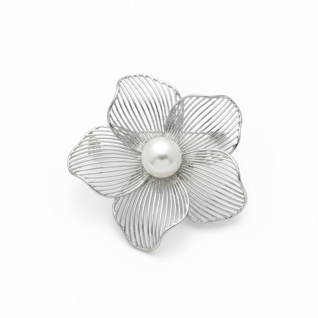 Silver flower-shaped brooch with a pearl center on a textured white surface